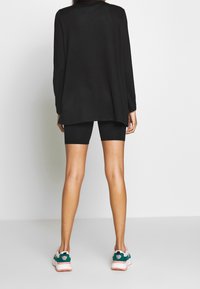 Černý dlouhý rukáv, oversized střih, kombinovaný s černými cyklistickými šortkami a vícemožnými atletickými botami se zelenými a růžovými akcenty.