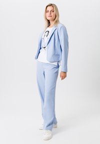 Lichtblauwe blazer en bijpassende broek van gladde stof, gecombineerd met een wit graphic t-shirt. Witte sneakers maken de outfit compleet.