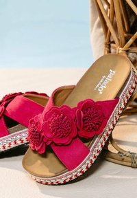 Rosafarbene Wildleder-Slidesandalen mit floralem Akzent, geflochtenem, raffia-ähnlichem Plateau und einer glatten, hellbraunen Fußbett. Mit dekorativen Perlendetails auf der Sohle.