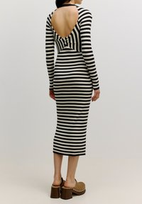 Schwarz-weiß gestreiftes, geripptes Langarmkleid mit einem Cutout-Detail am Rücken und einer Schleife, taillierte Silhouette, knielang, getragen mit Blockabsatzschuhen.