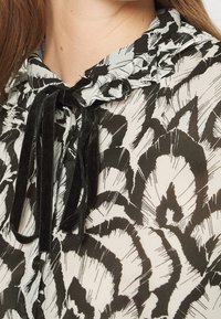 Blusa a strisce bianco e nero con colletto arricciato, dotata di un nastro in velluto, tessuto strutturato e dettagli con bottoni.