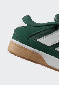 Green and white low-top sneaker with gum sole, padded collar, and perforated side panel details.