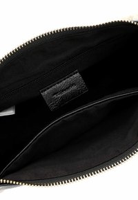 Clutch nera con zip, dotata di un'etichetta in pelle tessurizzata, con un interno in tessuto nero liscio e hardware della zip in colore oro.