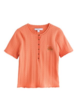 Top in maglia corallo a maniche corte con righe verticali strutturate, scollatura tonda, bottoni marroni e piccolo patch ricamato sul petto sinistro.