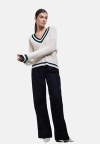 Leichtes Strickpullover in Creme mit grünem und schwarzem V-Ausschnitt, kombiniert mit dunklen, weiten Jeans und spitzen silbernenAbsätzen.