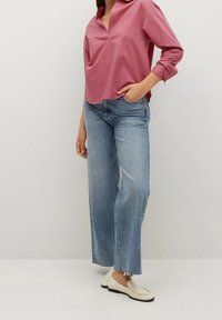 Chemise rose à col avec un col en V ; associée à un jean bleu clair à jambes larges ; chaussures plates crème avec des détails texturés.