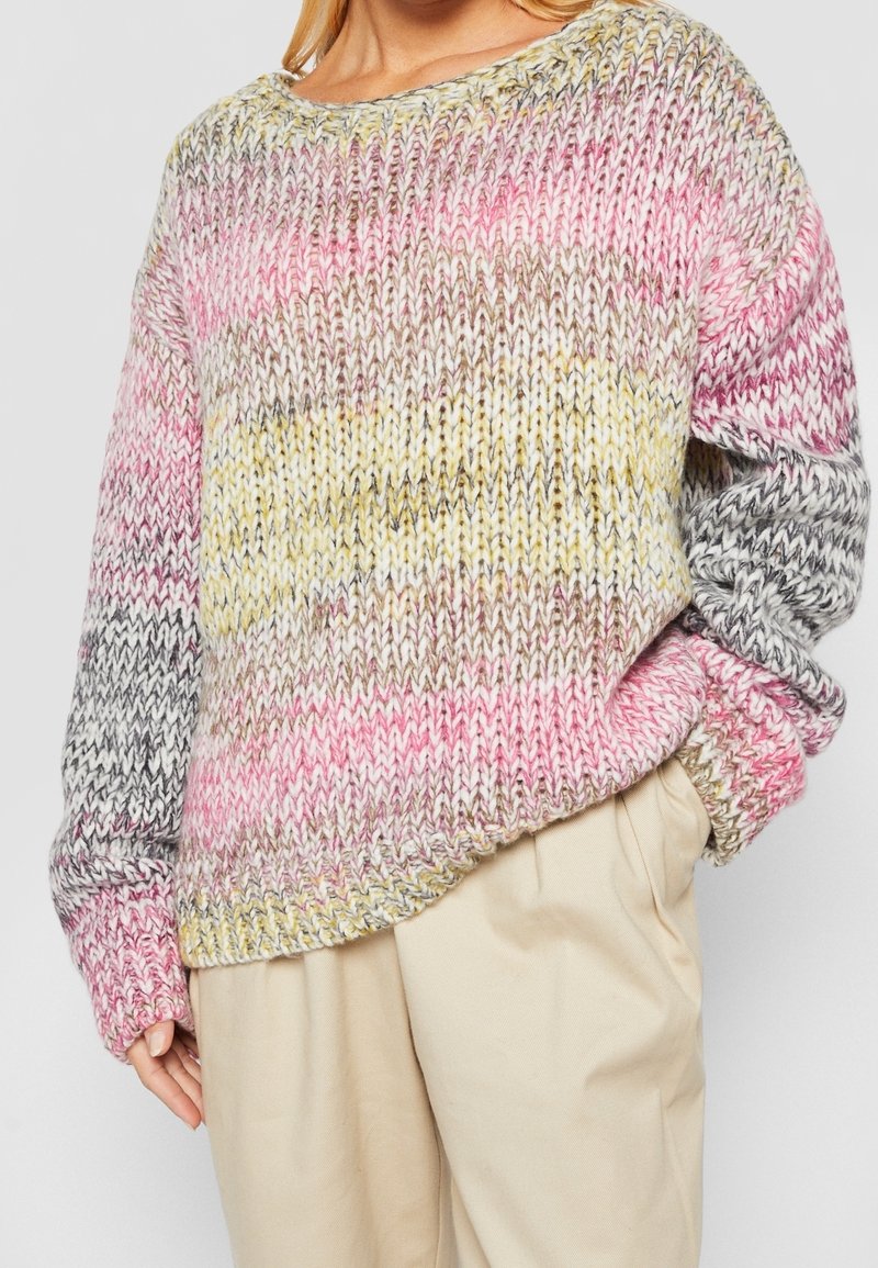 Pull en maille épaisse dégradé de rose, jaune et gris. Poignets et ourlet côtelés. Coupe ample. Porté avec un pantalon beige.