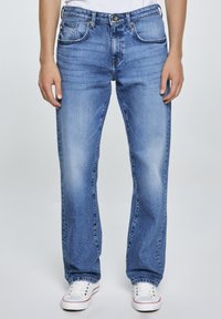 Sinised denimteksad sirge lõikega, klassikalise viie tasku paigutusega ja kulunud pesuga. Kombineeritud valgete madalate spordijalatsitega.