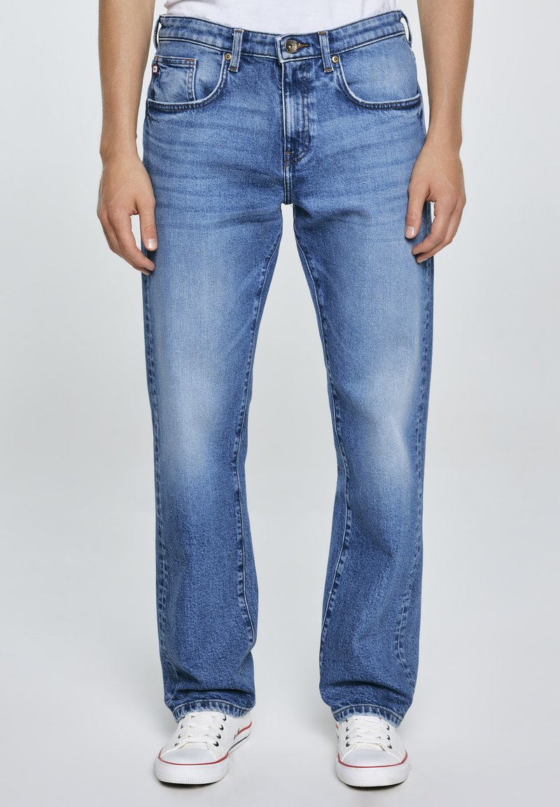 Sinised denimteksad sirge lõikega, klassikalise viie tasku paigutusega ja kulunud pesuga. Kombineeritud valgete madalate spordijalatsitega.