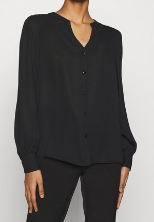 Zwarte blouse met een V-hals en lange, licht opbollende mouwen. Voorzijde met knoopsluiting en bijpassende knopen. Zachte, gladde stof zonder zichtbare patronen.