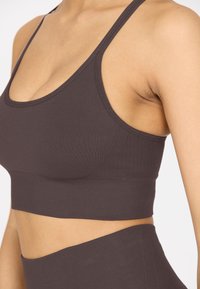 Braun Sport-BH aus glattem, elastischem Material. Mit rundem Ausschnitt, verstellbaren Trägern und geripptem Muster entlang des Bundes.