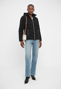 Veste en duvet noire avec couture en chevron, fermeture éclair et capuche ; associée à un jean droit bleu clair et des bottes noires à bout pointu.
