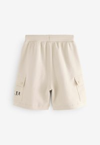 Beige Cargo-Shorts mit elastischem Bund, seitlichen Taschen und schwarzem Logodruck. Weicher Stoff mit glatter Textur und lässigem Design.