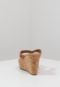 Klínová sandál s korkovou podešví, hnědým semišovým pásem a zaobleným zadním dílem. Texturovaný povrch, otevřený design podpatku a minimalistické detaily z kovu.