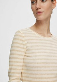 Top beige a costine con strisce orizzontali color marrone chiaro, dotato di scollatura rotonda e maniche lunghe, che presenta una texture morbida.
