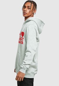 Ljust grå hoodie i mjukt tyg, med en framficka och röd grafisk textdesign. Inkluderar dragsko för huvan och ribbade muddar.