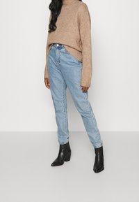 Jean taille haute bleu clair à coupe décontractée, associé à un pull en tricot beige et des bottines noires à talons. Tissu texturé.