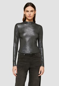 Schwarzes, glänzendes Langarm-Oberteil mit hohem Kragen, aus glitzerndem Material, kombiniert mit dunklen, geraden Jeans.