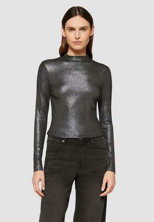 Glanzend zwart langarmtop met een hoge hals, gemaakt van een glinsterend materiaal, gecombineerd met donkere straight-leg jeans.