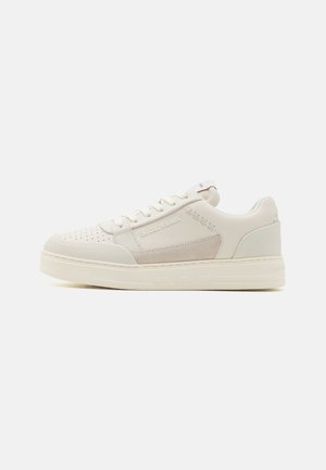 Baskets blanches avec une boîte à orteils perforée, tige en cuir lisse, accent en daim sur le côté, lacets plats et semelle en caoutchouc texturée.