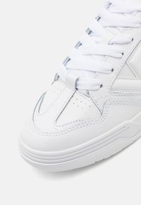 Sneaker bianco con tomaia in pelle testurizzata, dotato di una punta liscia, dettagli perforati e lacci bianchi. Suola in gomma con motivo di aderenza.