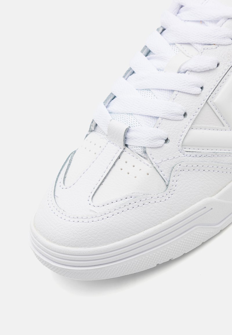 Baskets blanches avec une tige en cuir texturé, présentant un bout lisse, des détails perforés et des lacets blancs. Semelle en caoutchouc avec un motif de traction.