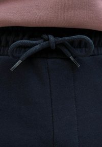Navy trekkoord tailleband met gevlochten textuur en plastic aglets, gecombineerd met een roze top met een gladde stoffen oppervlakte.