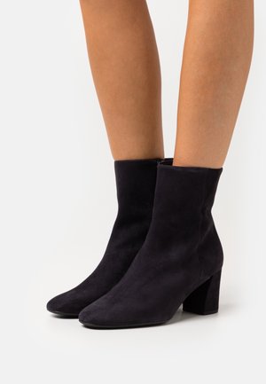 Stivaletti neri in suede alla caviglia con punta quadrata e tacco spesso. Il design è elegante e minimalista, caratterizzato da una texture liscia e senza hardware visibile.