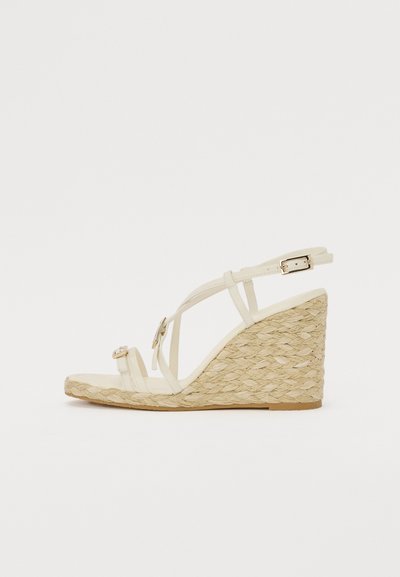 Sandales à talons compensés avec une semelle en jute tressé, des brides en ivoire et un petit détail de boucle métallique. Design minimaliste avec un embout ouvert.