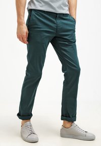 Teal färgade bomullschinos med en tapered fit, som har framfickor, bälteöglor och uppvikta fållar, tillsammans med ljusgrå sneakers.