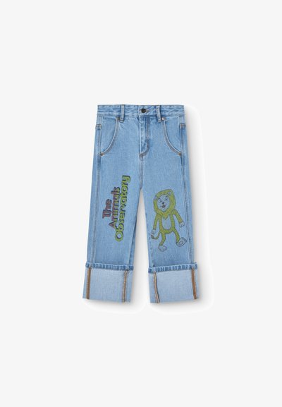 Light blue denim jeans with rolled hems, featuring green and red embroidered text and a cartoon lion with a green mane on one leg.