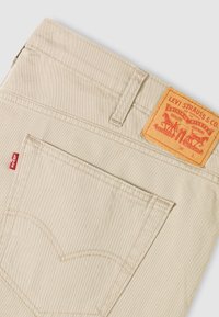 Pantalon beige Levi's montrant la poche arrière avec une étiquette rouge Levi's et une étiquette en cuir marron Levi Strauss & Co. au-dessus de la ceinture.