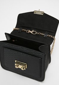 Czarna torebka z materiału sztucznego przypominającego skórę węża, z zapięciem w kolorze złotym, łańcuszkowym paskiem oraz czarną tkaniną wewnętrzną. Ma wyraźnie zarysowany kształt oraz kieszonkę wewnętrzną.