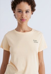 Světle žluté bavlněné tričko s kulatým výstřihem a krátkými rukávy. Na levé části hrudi je zelený nápis "Pepe Jeans". Měkká textura.
