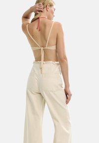 Beżowy szydełkowany biustonosz na cienkich ramiączkach z wiązaniem z tyłu. W komplecie z wysokimi spodniami w kolorze kremowym o szerokich nogawkach, z postrzępionymi nogawkami i kieszeniami z tyłu.