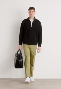 Svart zip-up sweatshirt, ljusgröna byxor, vita sneakers och bär en svart läderväska; minimalistsik design, släta texturer.