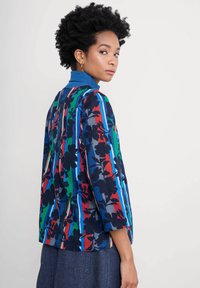 Blüemusterte Jacke in blau, rot, grün und grau gestreift; mit einem gerippten blauen Kragen und Dreiviertelärmeln; leichtes Material.
