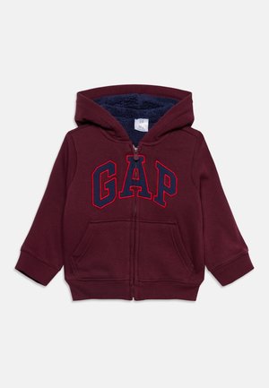 Bordová mikina na zips s kapucňou, modrým fleeceovým podšívaním, prednými vreckami a veľkým modro-červeným logom "GAP" na hrudi.