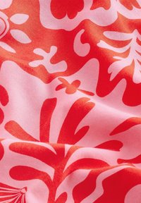 Gros plan sur un tissu avec des motifs floraux abstraits rouges et roses et des formes organiques sur une surface froissée.