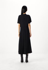 Schwarzes Midi-Kleid mit kurzen Ärmeln, einem hohen Kragen und einem Reißverschluss auf der Rückseite. Glatte Textur und lockere Passform, kombiniert mit kniehohen schwarzen Stiefeln.