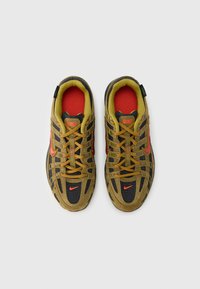 Buty sportowe Nike z brązowo-czarną siateczkową cholewką, żółtymi akcentami, czerwonym wykończeniem i pomarańczowym logo. Charakteryzują się misternym sznurowaniem i teksturowaną podeszwą.