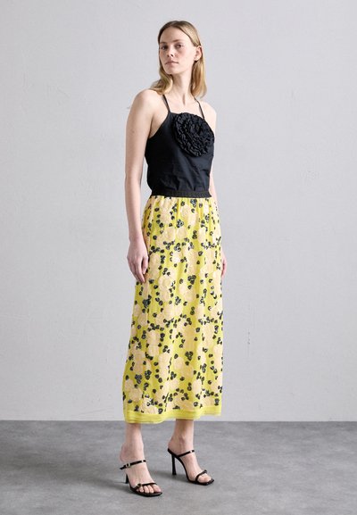 Black sleeveless top with a textured floral detail; yellow skirt with a floral pattern and green accents, paired with black strappy heels.