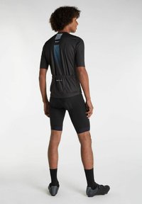 Mandens sorte cykeltrøje med korte ærmer har en struktureret blå lodret stribe, som er suppleret af sorte polstrede cykelshorts og cykelsko.