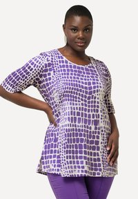 Top morado y blanco con un patrón, de manga corta, con escote redondeado y un corte suelto. Textura suave, presenta un diseño en forma de cuadrícula.