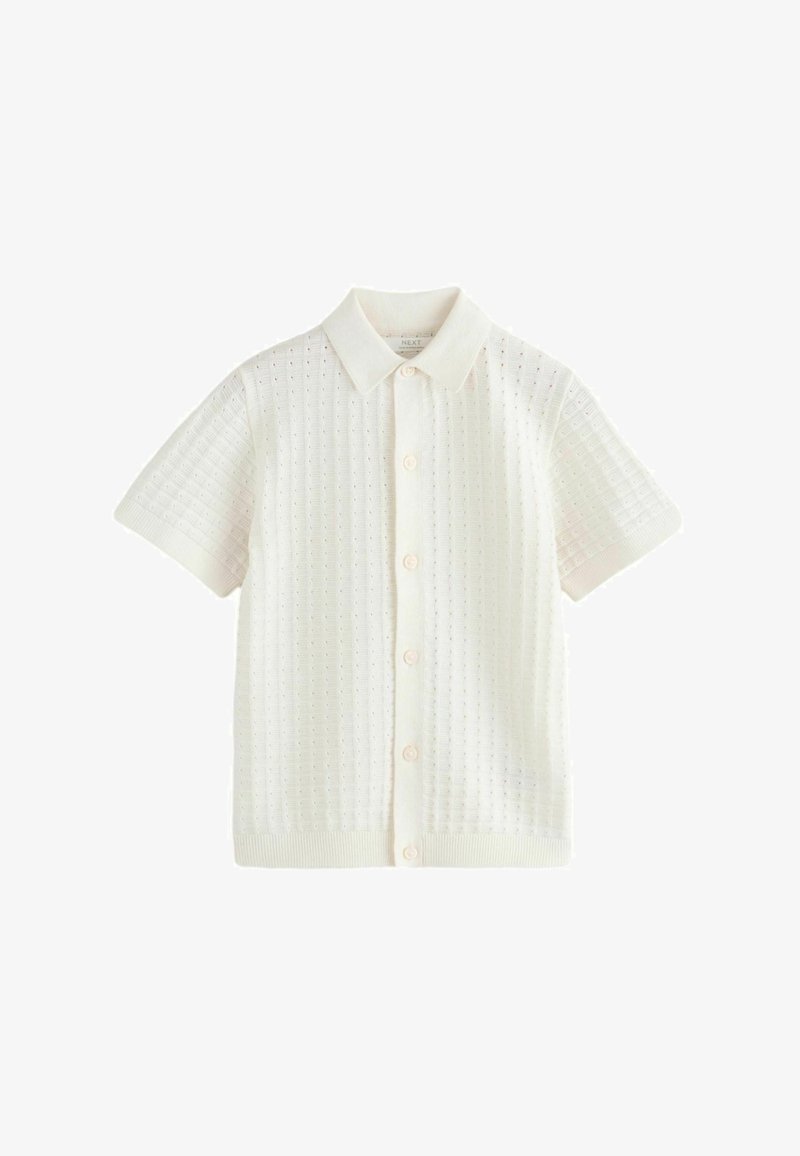 Kurzarm, cremefarbendes Hemd mit Knopfleiste aus gestricktem Stoff mit strukturiertem Muster, wobei der Kragen und der gerippte Saum hervorgehoben werden.