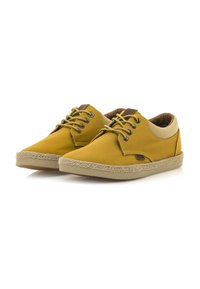 Zapatos de lona amarillos con un perfil bajo, cuello beige en contraste y detalle de suela de cuerda trenzada. Presentan cordones negros y una etiqueta de logo marrón.
