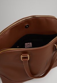 Brown faux leather handbag with gold zipper and hardware. Large compartment with a black interior and a small zip pocket inside.