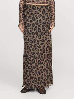 Maxi-Rock im Leopardenmuster aus einem transparenten, braunen Stoff mit schwarzen Punkten. Hat einen geraden Schnitt und einen leichten Rüschenrand am Saum. Trägt dazu schwarze Schuhe.