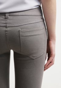 Grå denimjeans med en figurnära design, med bakfickor och platta sömmar, visade från baksidan.