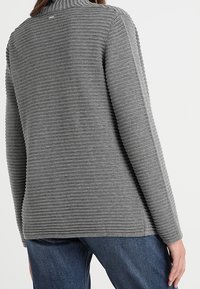 Pull en cou roulé texturé gris avec des nervures verticales, manches longues et ourlet arrondi. Présente un petit accent métallique au niveau du col à l'arrière.